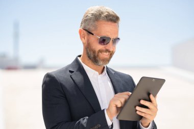 Açık havada tablet kullanan mutlu bir iş adamı. Tabletle başarılı bir iş adamı. Dışarıda tablet üzerinde çalışan bir iş adamı. Zarif iş adamı tableti kontrol ediyor. Dijital aygıt kullanan işadamı