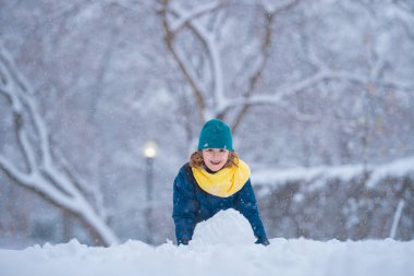 Karla oynayan çocuk, kar yağarken dışarıda. Kış çocuğu, açık hava portresi. Çocuk karda oynuyor. Kar parkında çocuk oyunu. Kış çocuğu suratı. Karda mutlu bir çocuk. Kış çocukları aktivitesi