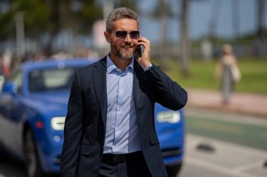 Takım elbiseli bir iş adamı. Lüks bir arabanın yanında zengin bir işadamı. Küresel. Başarılı bir iş. Pahalı arabanın önünde zarif bir iş adamı. Başarılı iş adamı