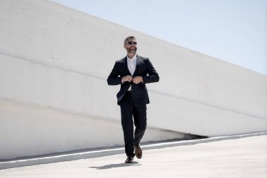 Dışarıda yürüyen bir iş adamı. Takım elbiseli başarılı bir iş adamı, tam boy. Takım elbiseli kendine güvenen bir iş adamı. İşadamı çekip gidiyor. Zarif takım elbiseli zengin adam. Kendine güvenen şehirli iş adamı.