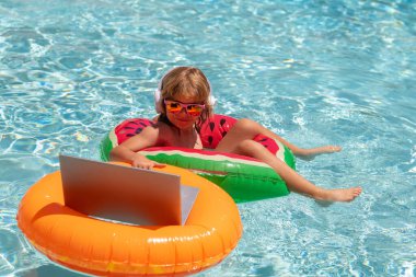 Yaz tatilinde dizüstü bilgisayarla çalışan çocuklar. Bilgisayar kullanan küçük bir serbest çalışan, yüzme havuzunda çalışan. Yaz ofisi ve serbest meslek konsepti