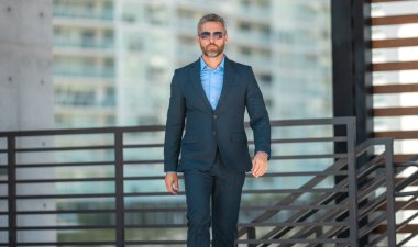 Başarılı bir iş adamı dışarıda yürüyor. Kendine güvenen bir iş adamı. Başarı işi. Takım elbiseli olgun iş adamı. Yakışıklı şirket lideri. Şehir ortamında zengin bir iş adamı. Zarif iş lideri.