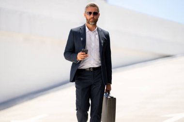 İş portresi. Dışarıdaki telefondan iş adamı aradı. Başarılı lider hareket halinde. Takım elbiseli, çantalı bir adam telefonda konuşuyor. İşadamı işe gidiyor. Çantası olan bir iş adamı. İş başarısı