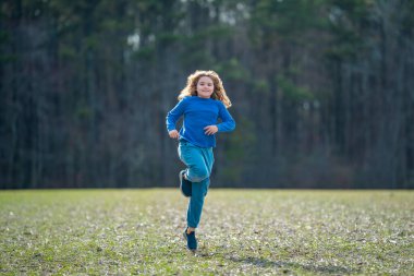 Çocuk sahada koşuyor. Dışarı koşan mutlu çocuk. Çocuk doğada zıplıyor ve koşuyor. Çocuk çayırda koşuyor. Aktif çocuklar için yaz eğlencesi. Neşeli çocuk özgürlüğü. Tasasız çocukluk.