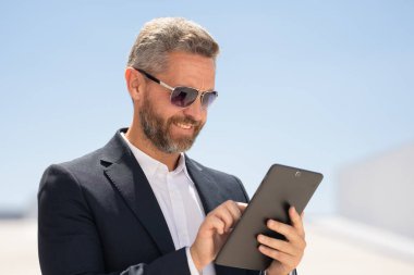 Açık havada tablet kullanan mutlu bir iş adamı. Tabletle başarılı bir iş adamı. Dışarıda tablet üzerinde çalışan bir iş adamı. Zarif iş adamı tableti kontrol ediyor. Dijital aygıt kullanan işadamı