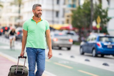 Bavullu bir turist sokaklarda yürüyor. Bir erkek turist, tropikal bir şehirde yaz tatilinin tadını çıkarır. Bavullu bir turist şehir manzarasını keşfediyor. Erkek turist şehirde yürüyor