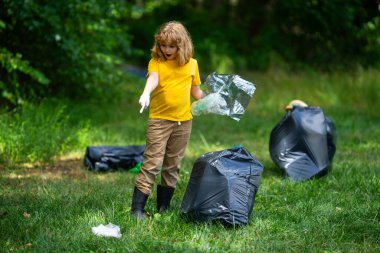 Lastik eldivenli çocuk çöp torbasıyla ormandaki çöpleri temizliyor. Eko, çevre koruma. Kirliliği geri dönüştür. Çocuk çöp ve plastik çöp topluyor. Çevreyi koru. Eko çocuklar