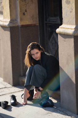 Açık havada topuklu ayakkabı giyen genç bir kız. Moda ayakkabıları gösteren şık bir genç. Genç model ciddi görünüyor. Gölgeli yüzlü genç kızın portresi. Gen Z yaşam tarzı ve şık ayakkabılar.