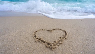 Kalp kumda çizilmiş. Dalgalar kalp şeklinde bir işaret oluşturuyor. Kumsalda aşk. Romantik yaz. Kumdan yapılmış bir kalp. Aşk ve okyanus dalgaları