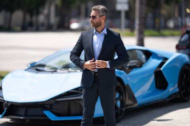 Olgun iş adamı. Zengin iş adamı başarının tadını çıkarıyor. Lüks bir iş. Pahalı arabanın önündeki zengin adam. Lüks iş seyahati. Klasik takım elbiseli, kendinden emin zengin bir iş adamı.