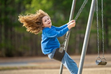 Çocuk parkta salıncakta sallanıyor. Sarı saçlı küçük bir çocuk salıncakta sallanıyor. Salıncakta gülümseyen mutlu çocuk. Mutlu çocukluk anları. Çocuk dışarıda oynuyor. Çocuk salıncakta eğleniyor. Çocuklar için açık hava oyunu