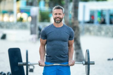 Halteri kaldıran formda bir adam. Halk parkında halterle ağırlık çalışması. Güçlü kollar ve omuzlar halteri kaldırıyor. Spor model halter yapıyor. Açık hava halterleri egzersizleri ile atletik yaşam tarzı