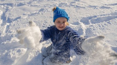 Çocuk kar atıyor. Kış eğlencesi. Kar atan mutlu çocuk. Çocuklar kartopu atarak karda oynarlar. Karda oynayan çocuk, kış doğasında tatil. Örgü şapkalı çocuğun kış portresi.