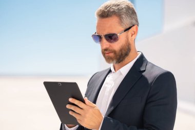 Ciddi bir iş adamı dışarıda tablet kullanıyor. Tabletle başarılı bir iş adamı. Dışarıda tablet üzerinde çalışan bir iş adamı. Zarif iş adamı tableti kontrol ediyor. Dijital aygıt kullanan işadamı