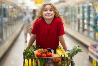 Sepetli çocuk sebze reyonunda. Çocuk markette meyve topluyor. Alışveriş arabalı çocuk. Çocuk süpermarkette alışveriş yapıyor. Çocuk sağlıklı ürünler alıyor. Marketteki çocuk.