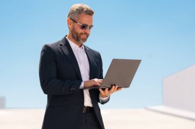 İş adamı dışarıda dizüstü bilgisayar kullanıyor. Dizüstü bilgisayar kullanan 40 'lı yaşlarda biri. Dizüstü bilgisayarı olan kendine güvenen bir iş adamı. İnternette iş. İş adamı laptoptaki verileri kontrol ediyor. Takım elbiseli iş adamı internette çalışıyor.