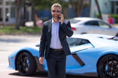 Zengin bir iş adamı. Zengin işadamı başarısının tadını çıkarıyor. Şık takım elbiseli lüks iş adamı. Pahalı arabanın önündeki zengin adam. Lüks iş seyahati. Klasik takım elbiseli, kendinden emin zengin bir iş adamı.