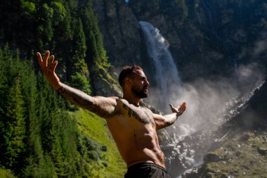 İnsan meditasyonu ve doğadaki refah. Çevrede özgürlük. Ormanda şelaleye karşı meditasyon yapan rahat bir adam. Özgürlük ve mutluluk yaşam tarzı. Sağlık kaplıcası, tatil ve yoga meditasyonu