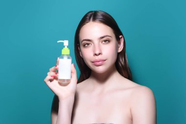 Stüdyoda cilt bakımı yapan güzel bir kadın var. Kadın yüzünün yanında kozmetik tüpü. Güzellik ürünüyle bir kızın portresi. Su şişesi olan bir kadın model. Kadın yüzü ve makyaj malzemeleri.