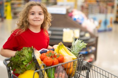 Markette alışveriş arabasıyla çocuk alışverişi. Çocuk markette taze sebze seçiyor. Markette yiyecek alışverişi yapan çocuk. Yerel bir dükkanda sağlıklı ürünler seçen bir çocuk. Bakkalda taze yiyeceği olan çocuk.