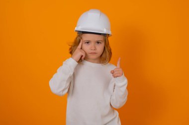 Kasklı, inşaatçı üniformalı bir çocuk. Mühendis kılığında kask takan mutlu çocuk. Becerikli çocuk. Çocuk inşaat işçisi. Çocuk müteahhit. Tamirci kıyafeti giymiş çocuk.