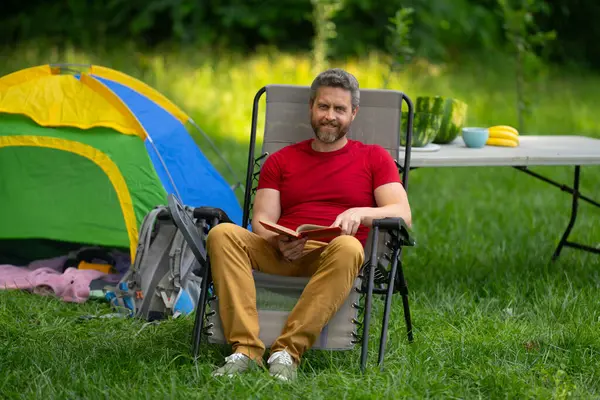Turistler doğada kamp yapmayı seviyor. Doğaya yaz gezisi. Orman kampında dinlenen adam. Kamp gezisi. Yürüyüşten sonra çadırın yanında dinleniyor. Barışçıl bir kamp alanında özgürlük tatili. Yazın piknikteki adam