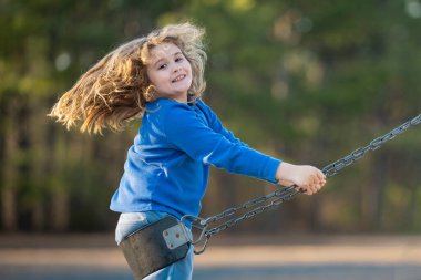 Heyecanlı çocuk eğleniyor. Çocuk bahçesinde mutlu bir çocuk. Havada sallanan tasasız çocuk. Mutlu çocuklar dışarıda oynuyor. Genç çocuk heyecanla sallanıyor. Dışarıdaki oyuncu çocuk. Komik çocuk yüzü.