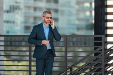 İş adamı telefonda konuşuyor ve yürüyor. Kendine güvenen bir iş adamı telefonla dışarı çıkar. İş telefonu konuşması. Şirket lideri telefonda konuşmakla meşgul. Zengin iş adamı. İş çağrısı