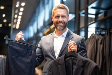 Takım elbiseli, butikte şık bir adam. Bir iş adamı mağazada şık bir takım elbise seçer. Modayı takip eden bir müşteri resmi kıyafet alırken ceketi inceler. Klasik kıyafetli çekici bir manken.