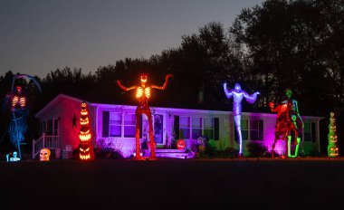 Cadılar Bayramı evinin dışında ürkütücü bir dekor var. Ön bahçede korkunç bir iskelet var. Ürkütücü fenerler ve balkabaklarıyla dekore edilmiş bir ev. Cadılar Bayramı süsü verandada. Geceleri ürpertici ev görüntüsü