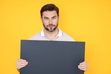 Stüdyo arka planında boş afiş olan bir adam. Elinde boş poster tutan çekici bir adamın portresi. Boş poster gösteren bir adam. İşaret panosu, pano ya da pano ile kopyalama alanı sunuluyor