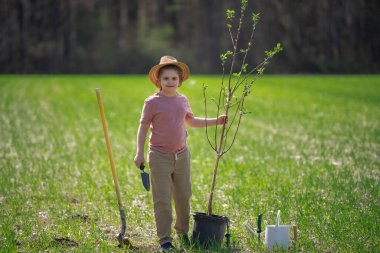 Kürekle ağaç yetiştiren çocuk. Arka bahçeye çocuk dikme ağacı. Bahar tarlasında çocuk dikimi. Sulama kutusu ve küreği olan küçük bahçıvan.