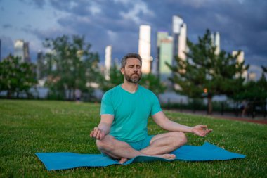 Hispanik Adam dışarıda otların içinde meditasyon yapıyor. Sporcu şehir parkında yoga yaparken asana meditasyonu yapıyor. Atletik erkek meditasyonu, rahatlama, sağlıklı yaşam tarzı kavramı. Açık havada meditasyon.