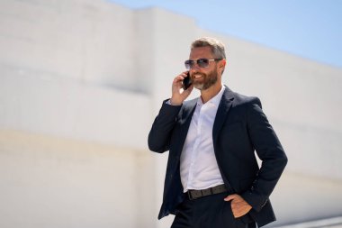 Ofis çalışanı dışarıda cep telefonuyla konuşuyor. Cep telefonunda iş adamı konuşması. İş adamı telefon görüşmesi yapıyor. Şık bir iş adamı telefon kullanıyor. İş görüşmesi. Meşgul işadamı telefonda konuşuyor.