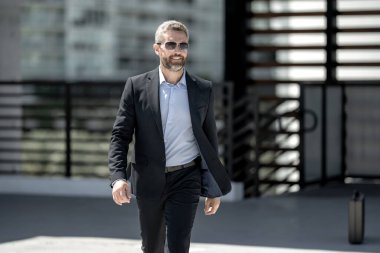 Başarılı bir iş adamı dışarıda yürüyor. Kendine güvenen bir iş adamı. Başarı işi. Takım elbiseli olgun iş adamı. Yakışıklı şirket lideri. Şehir ortamında zengin bir iş adamı. Zarif iş lideri.