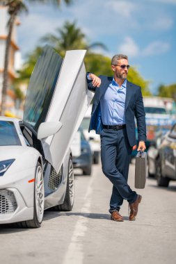 Lüks bir arabanın yanında zengin bir işadamı. Zengin bir iş adamı. Zarif zengin iş adamı. Pahalı arabası olan bir patron. Premium arabada duran zengin bir iş adamı. İş başarısı. Zenginlik kavramı