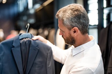 Bir butik danışmanı müşterinin mükemmel takımı bulmasına yardım eder. Lüks bir giysi koleksiyonu. Zarif takım iş adamı için mükemmel. İyi dikilmiş bir takım.