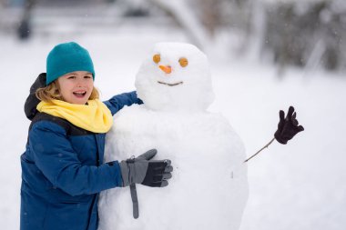 Çocuk kışın kardanadamla oynuyor. Kış günü havuç burunlu bir kardan adam. Kardan adam yapan çocuk. Kar parkında kardan adam yapan küçük çocuk. Karlı kış parkında kardan adamı kucaklayan çocuk