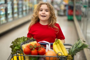 Süpermarkette el arabasıyla alışveriş yapan çocuk. Çocuk markette taze sebze seçiyor. Yiyecek satan bir çocuk. Markette ürün seçen bir çocuk. Bakkalda taze yiyeceği olan bir çocuk.