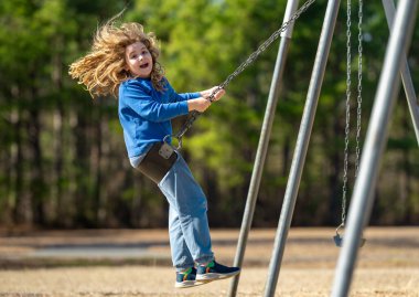 Bahar parkında sallanan neşeli çocuk. Sarı saçlı küçük bir çocuk salıncakta sallanıyor. Parkta gülümseyen mutlu çocuk. Mutlu çocukluk anları. Çocuk dışarıda oynuyor. Çocuk salıncakta eğleniyor. Çocuklar için açık hava oyunu
