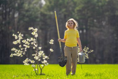 Çocuk bahçeye ağaç dikiyor. Çocuk kürekle toprak kazıyor ve ağaç dikiyor. Çocuk bahçıvan meyve ağaçlarıyla ilgileniyor. Çocuklarla ağaç dikmek. Yeşillik arayan bir çocuk. Çocuklar için bahçe.