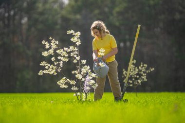 Arka bahçede küçük bir yardımcı. Çocuk ağaç dikiyor. Çocuklar için açık hava bahçıvanlığı. Genç bir bitkiyi suluyor. Çocukluk gelişimi. Çocukların ağaç diktiği bir çiftlik hayatı. Meyve Bahçesi