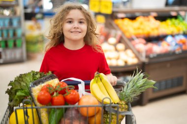Markette alışveriş arabasıyla çocuk alışverişi. Çocuk markette taze sebze seçiyor. Markette yiyecek alışverişi yapan çocuk. Yerel bir dükkanda sağlıklı ürünler seçen bir çocuk. Bakkalda taze yiyeceği olan çocuk.