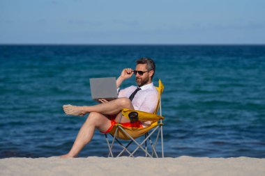 Deniz sahilinde dizüstü bilgisayar kullanan iş adamı. Yaz tatilindeki çılgın iş adamı. Heyecanlı iş adamı, çılgın komedi dünyası konsepti. Uzaktan kumanda çalışıyor. Yaz iş hayalleri