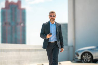 Başarılı bir iş adamı telefonu açık havada tutar. İş adamı dışarıda telefonda konuşuyor. Takım elbiseli olgun iş adamı. Şirket işi. Takım elbiseli zengin iş adamı. Açık hava iş portresi