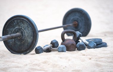 Kettlebell ve ağırlık arka planı. Ağır ağırlıklarla vücut geliştirme. Dambıllarla park egzersizi. Ağırlıklarla spor sahnesi. Kettlebell, halterler ve halterler. Kumsalda ağırlık çalışması.