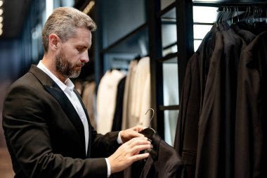 İş adamı için uygun. İyi giyimli bir erkek model bir butikte poz veriyor. Perakende satış elemanı şık bir adamın mükemmel takımı bulmasına yardım eder. Bir mağaza müdürü şık bir takım elbise ayarlar.