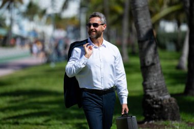 Sıcak iş. Yaz işi. Palmiye ağaçlarındaki iş adamı. Yazın iş adamı. Tatilde olan olgun bir girişimci. Tarz sahibi iş adamı açık hava portresi. Sıradan giyinen yakışıklı iş adamı.