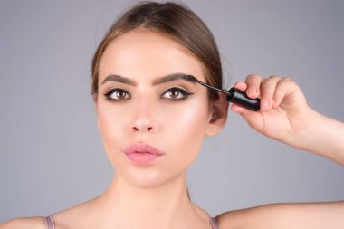 Eyebrow shaping, woman combs eyebrows with a brus. Eyebrow line. Makeup and cosmetology concept. Female model with long eyelashes and thick eyebrows. Perfect shaped brow