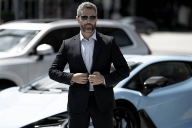 Lüks bir arabanın yanında zengin bir işadamı. Zengin bir iş adamı. Zarif zengin iş adamı. Pahalı arabası olan bir patron. Premium arabada duran zengin bir iş adamı. İş başarısı. Zenginlik kavramı